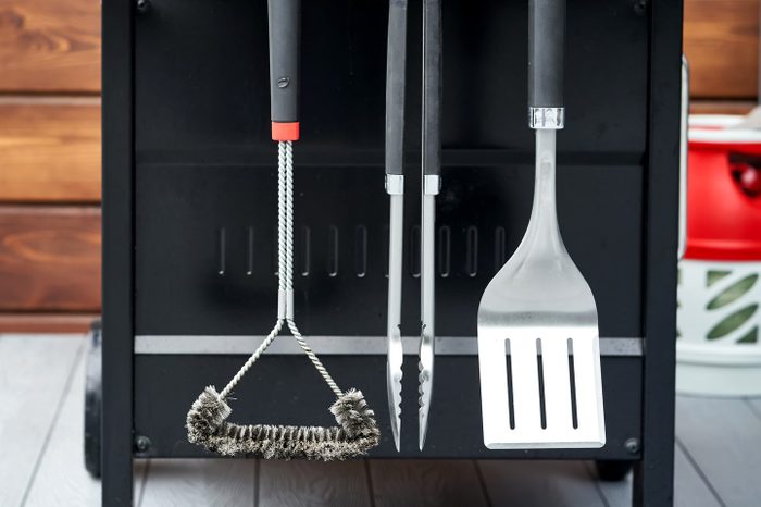 The grill utensils hang on the gas grill: a spatula, tongs, and a brush.