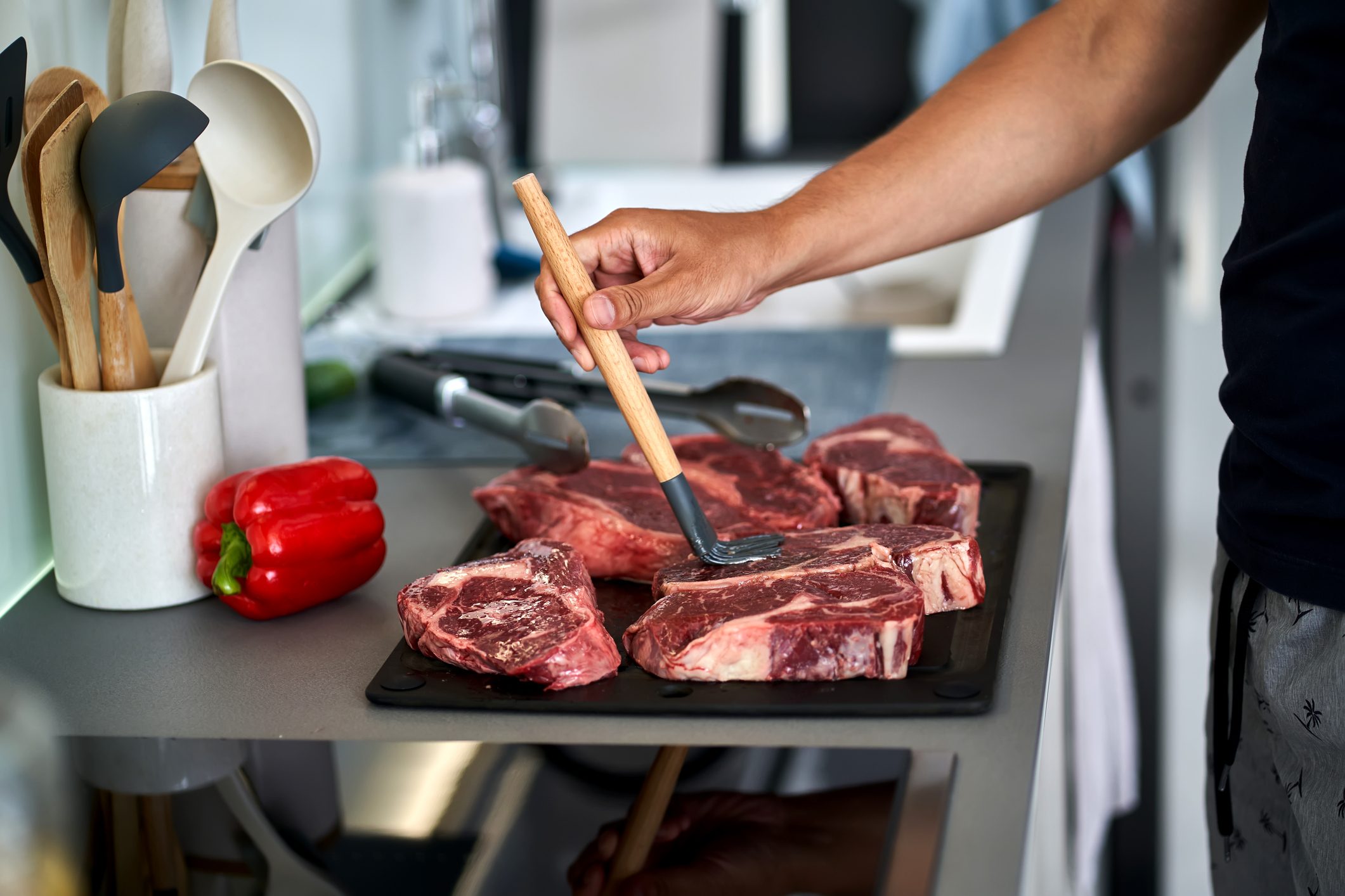 Men's hands lubricate meat steaks with oil before cooking.