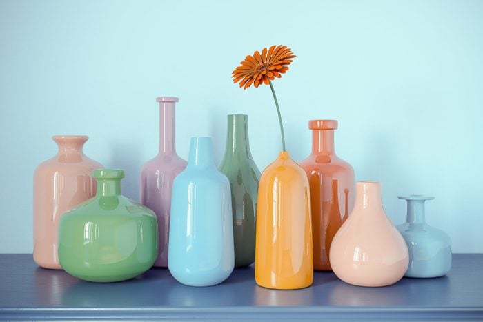 Multicolored Bottles Vases from Glass with one Daisy Flower on Blue Dresser and Blue Wall Abstract Background. 3D Rendering. Vintage Retro Colored