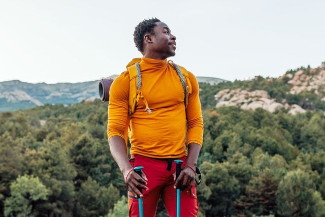 man Hiking while camping wearing an orange shirt, red pants, a backpack and trekking poles