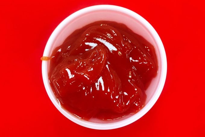 small paper dish of ketchup on a red background
