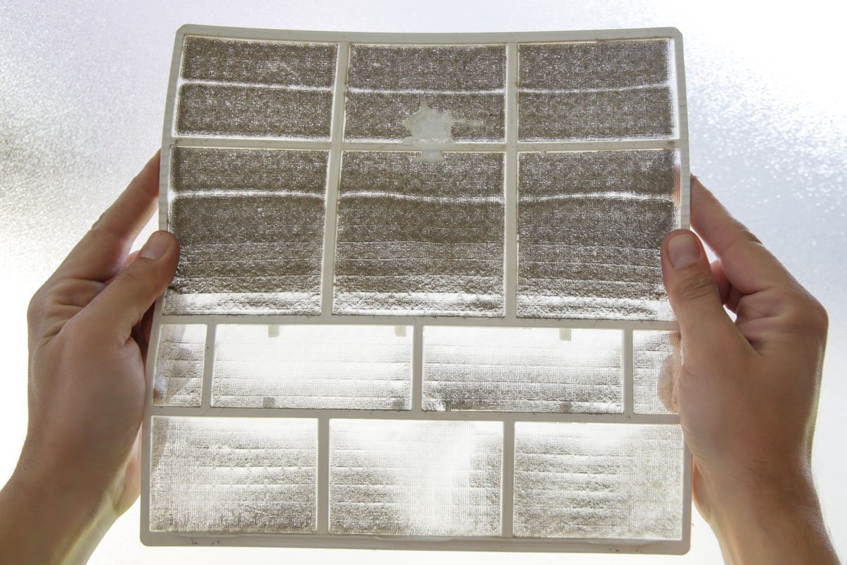Man Holding Very Dirty Air Conditioner Filter against the light to spot dust and debris in the filter