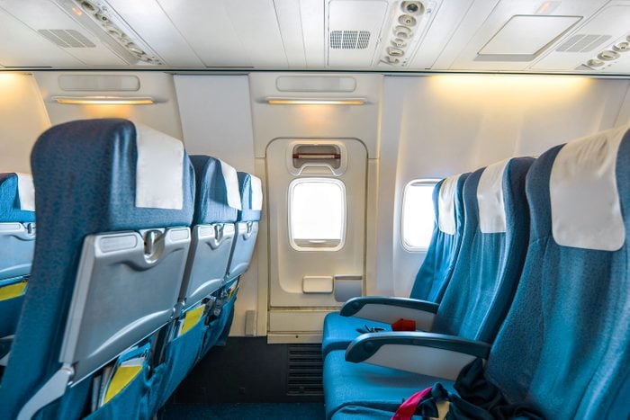 Comfortable Seats In Cabin Of Huge Aircraft With Screens In Chairs Back, emergency exit door and seat trays pictured in a bright cabin