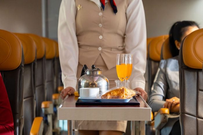 Airplane Flight attendant pushing the cart on aisle for serving food and drink to passengers in airplane cabin