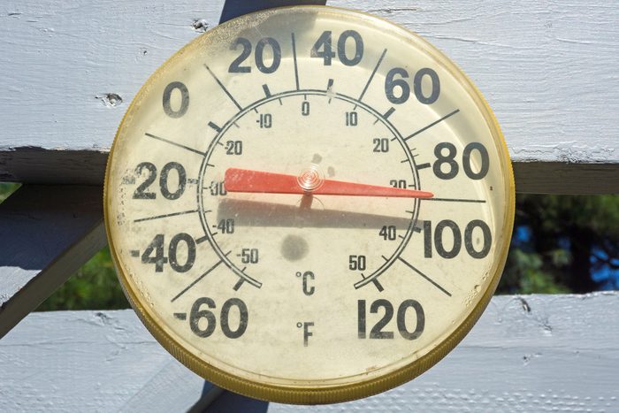 An old worn outdoor thermometer showing ninety degrees in full sunlight
