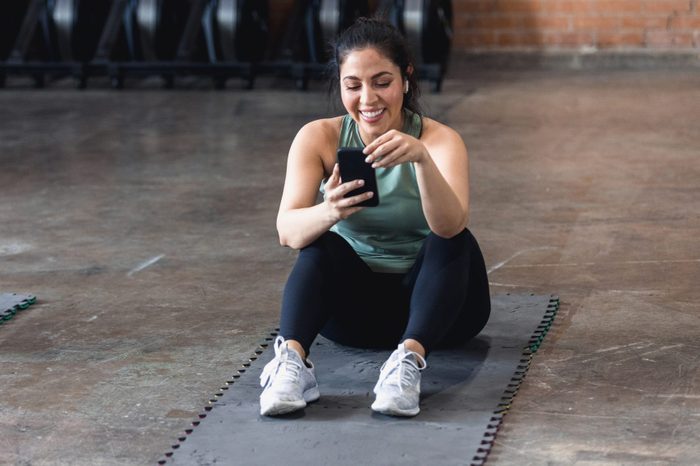 Woman sitting on exercise mat enjoys social media before workout