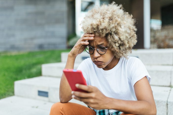 Afro woman looking worried and stress while reading bad news on her mobile phone.