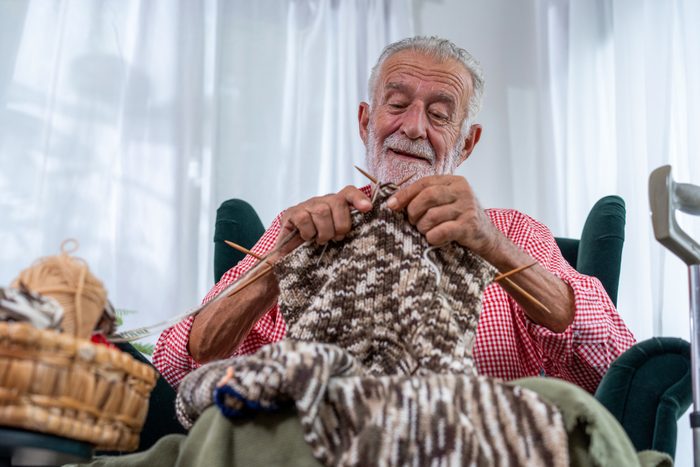 Senior man sitting in a wheelchair and knitting while relaxing at home.