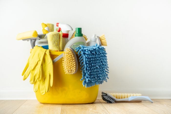 Brushes, bottles with cleaning liquids, sponges, rag and yellow rubber gloves on white background. Cleaning supplies in the yellow bucket on the wooden floor. Cleaning company service advertisement
