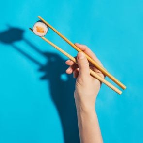 Hand demonstrating how to use chop sticks with chopsticks holding salmon maki sushi roll on a blue background
