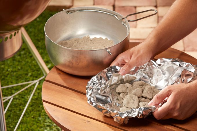 hands placing cooled charcoals in aluminum foil for disposal