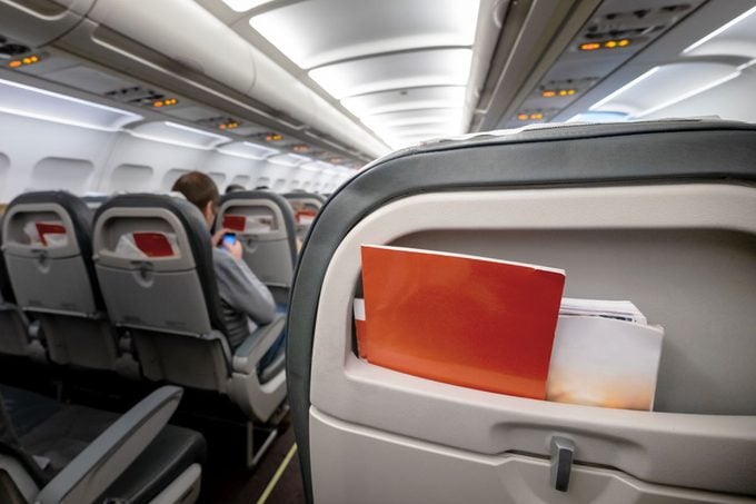 Back Of A Passenger Plane Seat with Brochures and an unknown passenger out of focus in the airplane