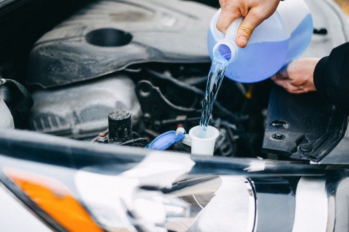 anonymous man's Hands Pouring Windshield Washer Fluid Into A Car's Tank in autumn to prep his car for the winter