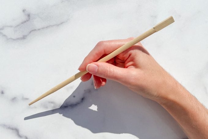 hand holding one chopstick over marble background to demonstrate How To Eat With Chopsticks step 2