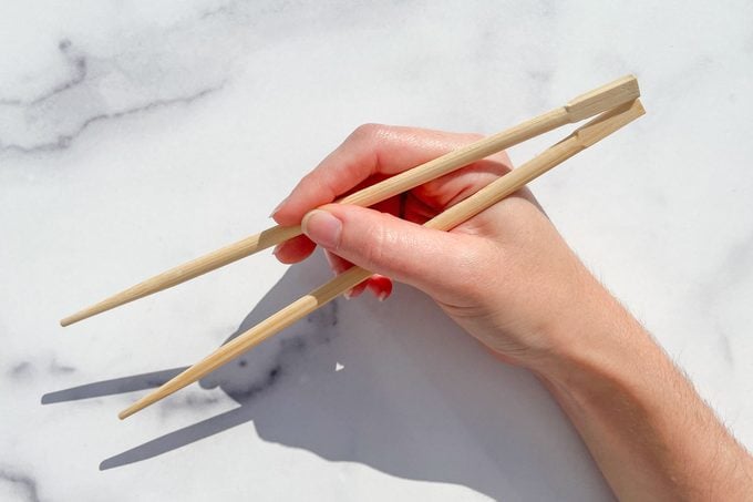 hand holding chopsticks over marble background to demonstrate How To Eat With Chopsticks step 3