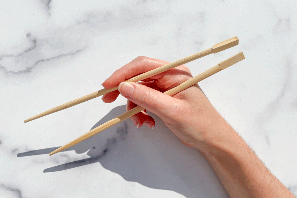 gif of hand holding chopsticks over marble background to demonstrate How To Eat With Chopsticks step 4