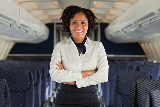 Smiling Stewardess Poses and Crosses Her Arms While Smiling on airplane in aisle inbetween of airplane seats