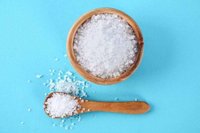 Sea salt in a wooden bowl and spoon on a blue table