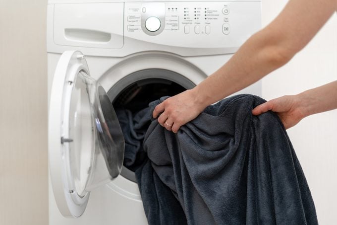 Photo of woman hands putting blanket in washing machine