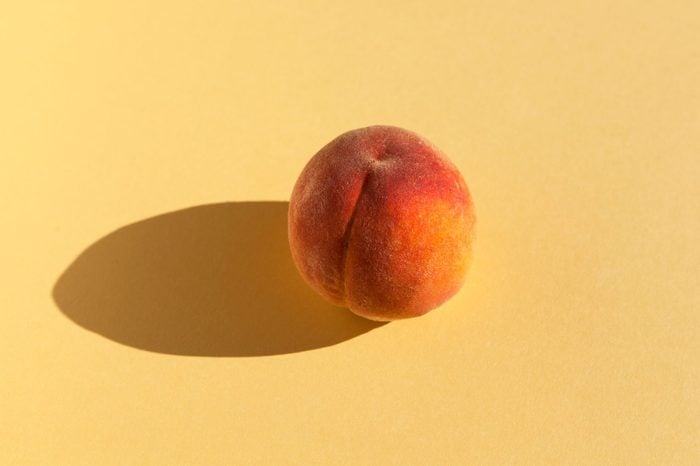 Ripe juicy nectarine or peach casts a shadow from sunlight on a yellow pastel background. Place for text