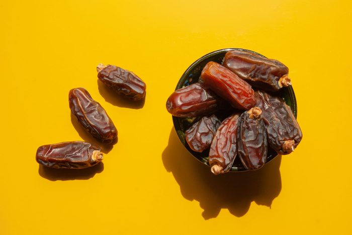 dried dates in bowl and scattered around on yellow ground