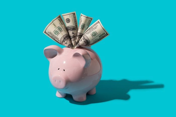 Piggy bank stuffed with hundred dollar bills on blue background with hard shadow