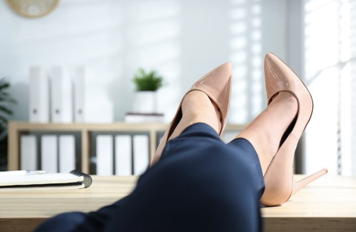 Lazy Female worker with high heels and feet on desk in office setting