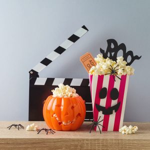 Horror movie night and Halloween party concept with jack o lantern pumpkin, popcorn and movie clapperboard on wooden table
