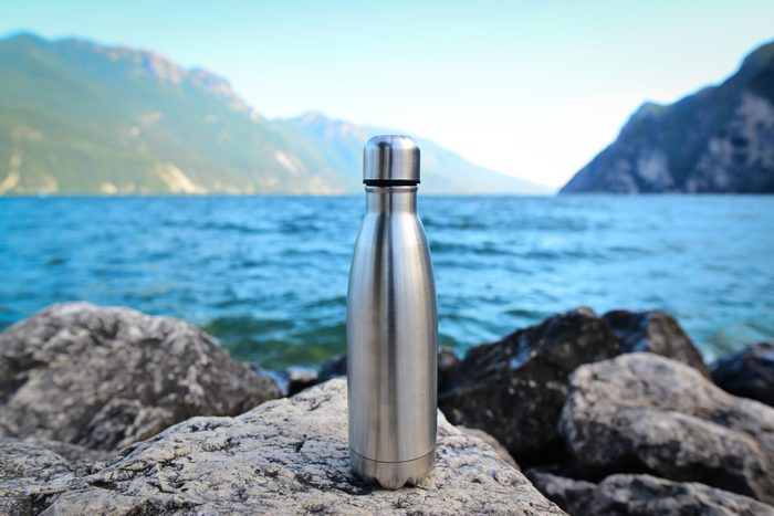 Steel eco thermo water bottle on the background of the lake in the mountains