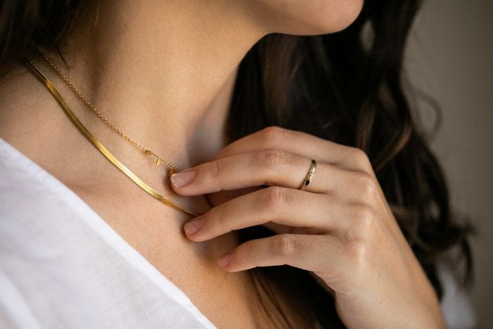 close up of a woman wearing a gold ring touching her gold necklace