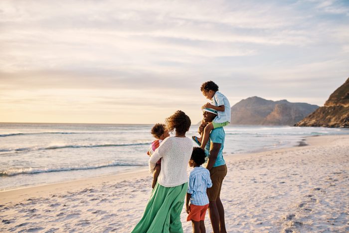 Happy family admiring the sunset view at the beach with copyspace. Relaxing during a summer vacation and enjoying the scenic landscape with calm waves. Loving parents bonding with their little kids