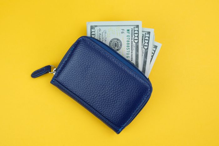 Small travel wallet and dollar bills sticking out of it on a yellow background