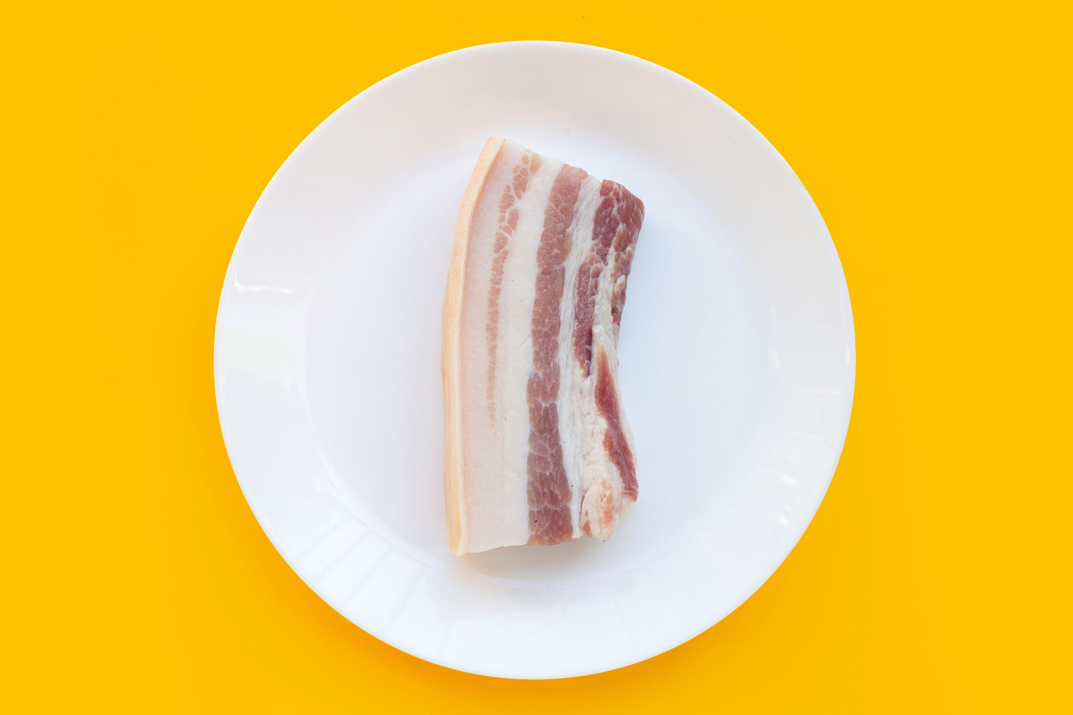 Streaky pork in white plate on yellow background.