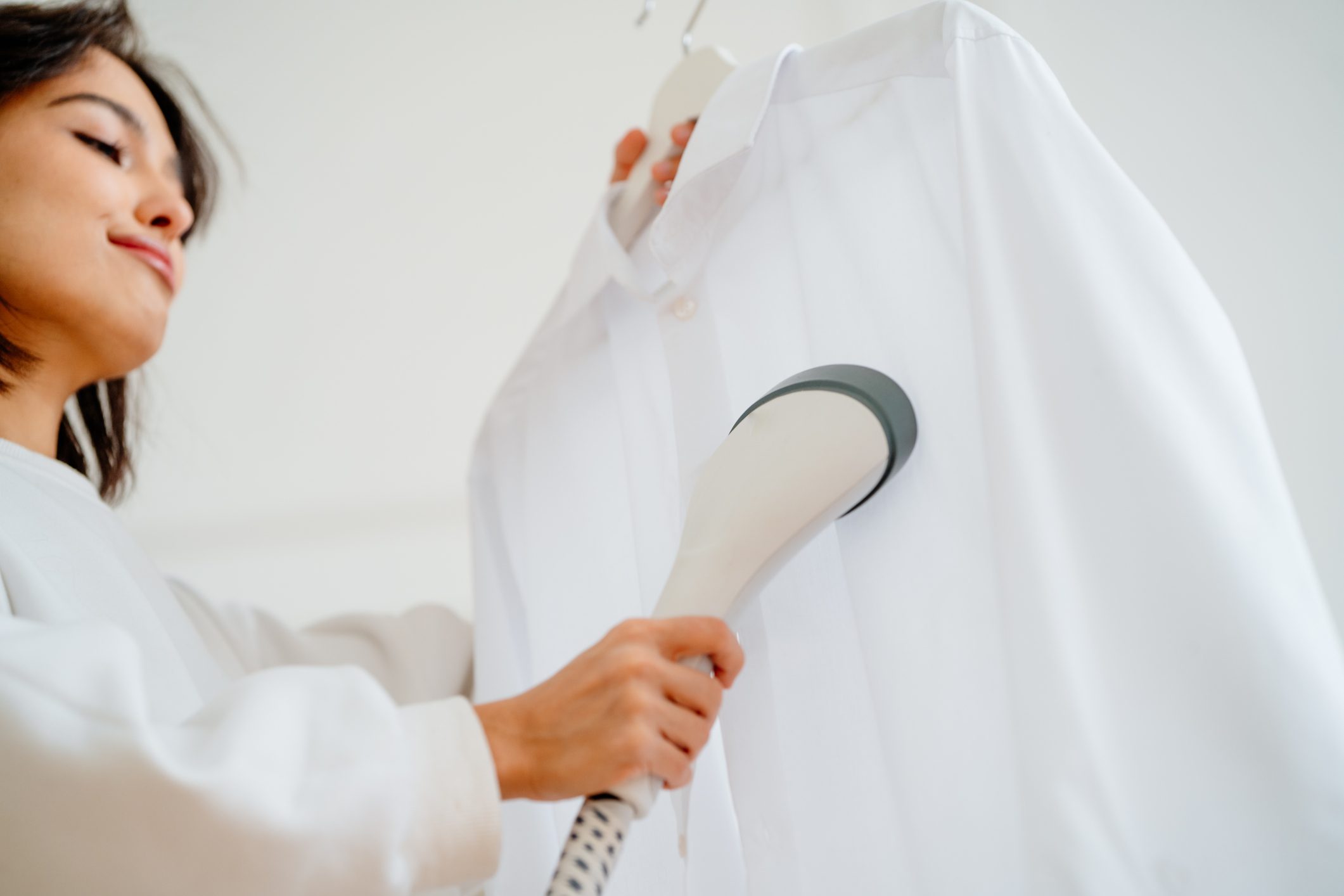 Woman using clothes steamer machine for removing wrinkles and folds from a white shirt