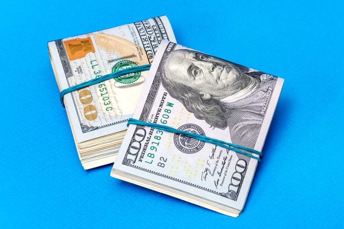 Two packs of folded dollar bills with rubber band on a blue background.