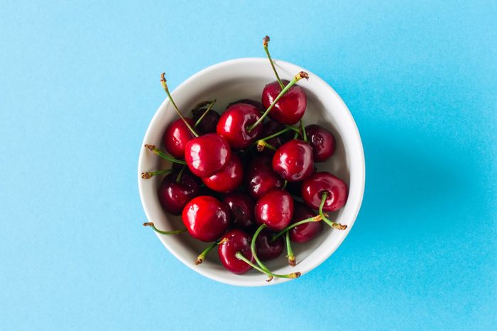 Heap of fresh ripe red cherries in a white bowl on a light blue background. Top view and copy space. Organic food concept.