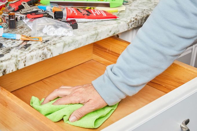 hand cleaning the drawer with microfiber cloth with items piled on the counter nearby
