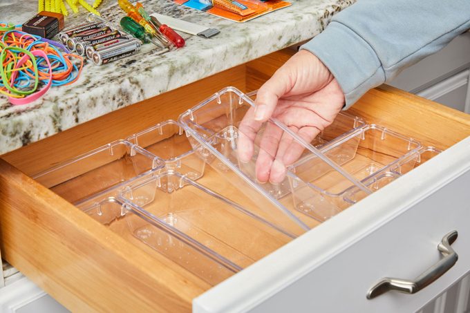 hand adding clear bins into the drawer with piles of organized items on the counter nearby