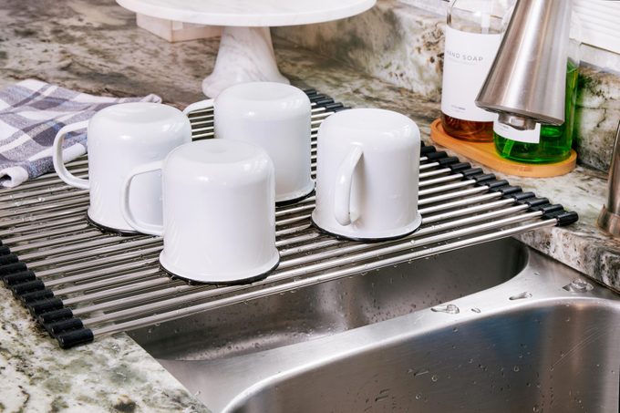 white mugs and cups drying on a over the sink dish rack