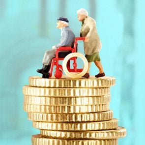 two elderly figurines on a stack of gold coins, turquoise background