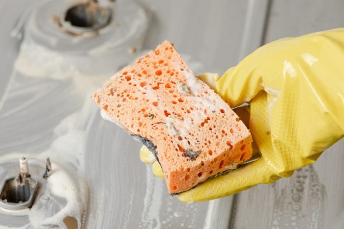 A hand in a yellow glove holds a dirty sponge.