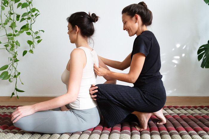 Latina female massage therapist giving upper back massage to woman. Thai massage technique for shoulder blade.
