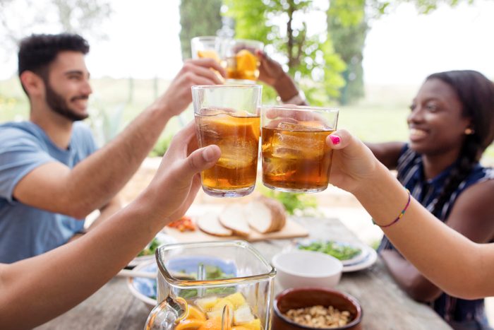 Friends toasting iced tea glasses at outdoor table on a sunny day