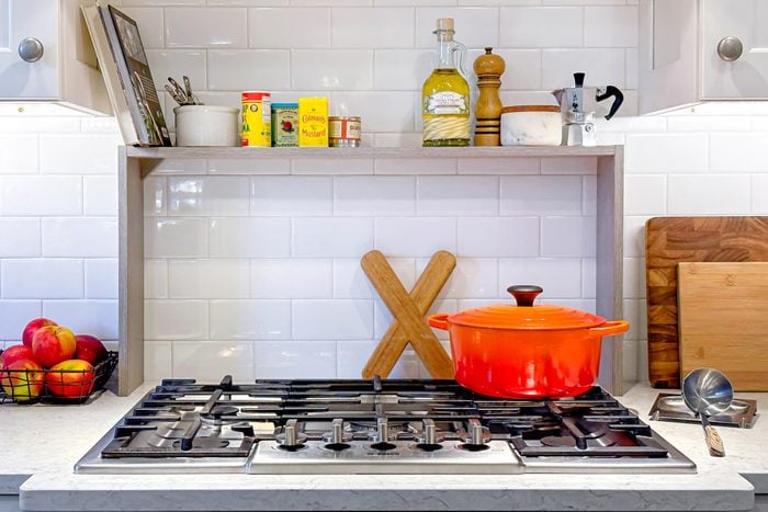 shelf over a stove in a kitchen with an orange dutch oven on the stove top