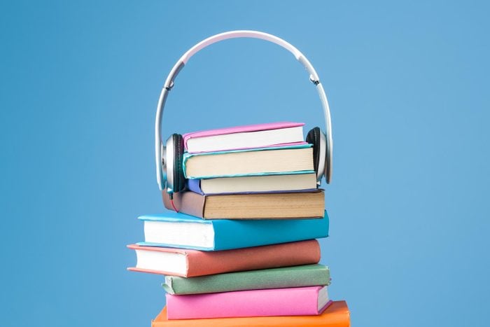 Headphones On Top Of Multicolored Hardcover Books For Audio Reading against a bright blue background