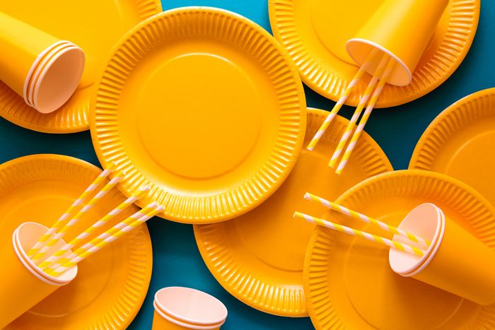 yellow disposable party supplies, paper plates, cups, straws, arranged on blue background