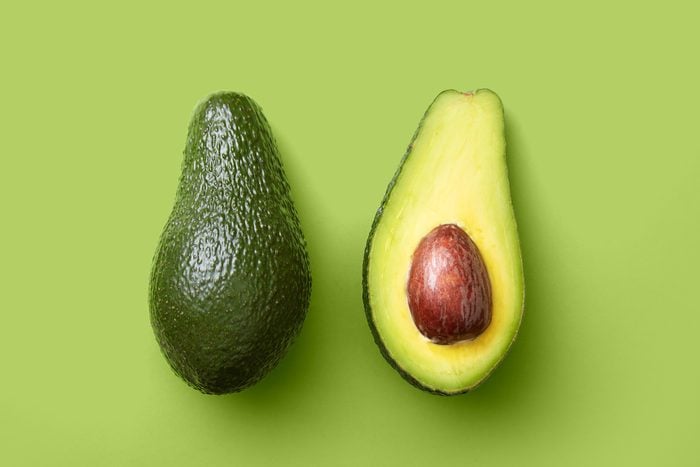 Avocado sliced half and whole on a green background viewed from above. Top view