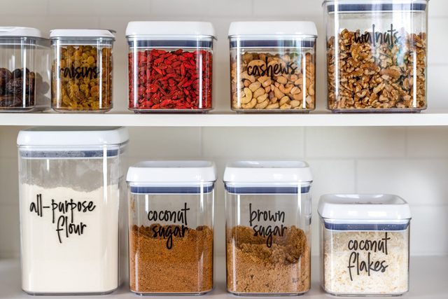 Neatly organized and labeled baking ingredients in BPA-free plastic storage containers in a kitchen cabinet