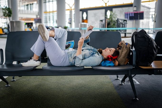 Young Woman waiting for delayed flight and reading digital book on chairs