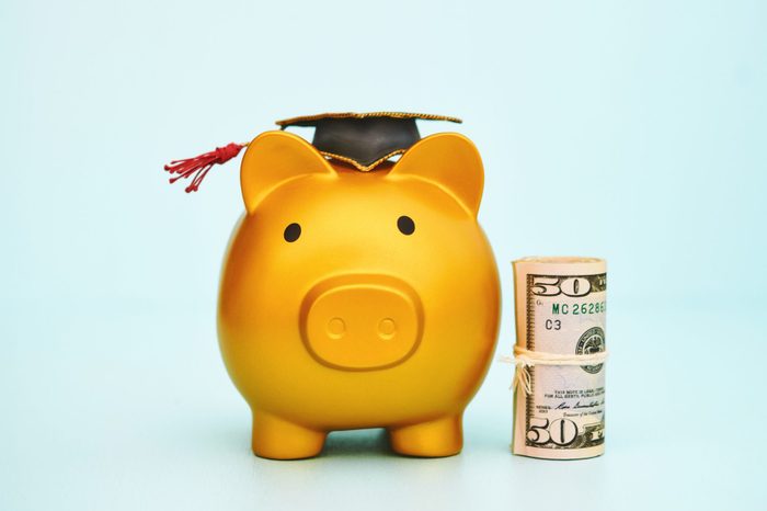 Cute gold colored piggy bank wearing a graduation cap and standing next to a roll of dollars. Education cost theme